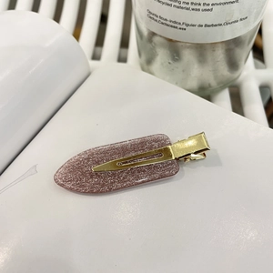 Nahaufnahme einer lila Glitzer-Haarspange mit goldenem Metallboden auf einer Buchseite