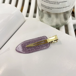Detailansicht einer lila glitzernden Haarspange aus Harz mit einer goldenen Entenschnabelklemme