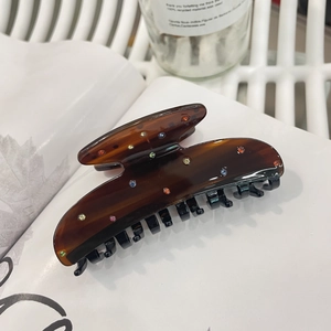 Brown acetate hair claw clip with colorful rhinestones on a white magazine background