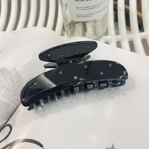 Black acetate hair claw clip with colorful rhinestones on a white magazine background
