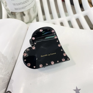 Détail d'une pince à cheveux coeur noire avec strass roses et lettrage doré sur un livre