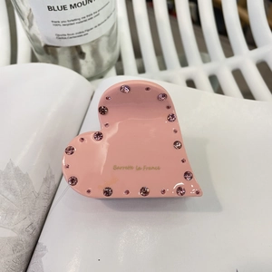Pince à cheveux coeur rose en acétate avec strass et texte doré sur un livre blanc