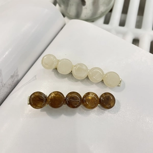 Minimalist resin bead hair clips in cream and amber brown on a white magazine background