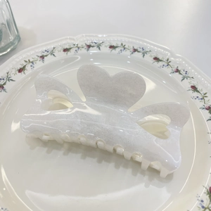 Pearly white glitter heart-shaped hair claw clip with cutout design on ceramic plate