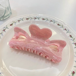 Pink heart-shaped hair claw clip with marble texture and gold glitter in a ceramic dish