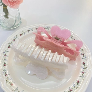 Sparkly acrylic heart claw clips in pink and white on a decorative ceramic dish