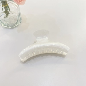 Dettaglio molletta per capelli con texture marmo bianco e finitura madreperla su fondo bianco