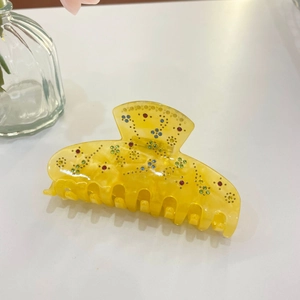 Close-up of a yellow acetic acid hair claw clip with colorful rhinestones in flower patterns
