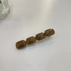 Détail de la pince à cheveux ambrée en résine avec clip en métal doré sur fond blanc