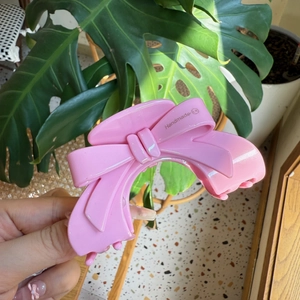 Pink acetate bow hair claw clip with handmade engraving held against green leaves