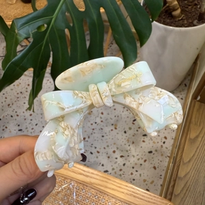 Detail of a handmade cream and green acetate hair claw clip with a 3D bow design