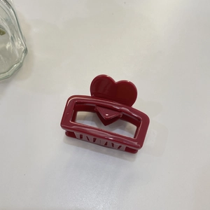 Macro detail of a dark red heart-shaped acetate claw clip on a minimalist white surface