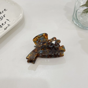 Detail of tortoiseshell hair claw with a crystal-centered flower on a minimal background