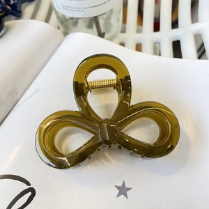 Close-up of semi-transparent dark olive green bow-shaped hair claw clip with golden spring