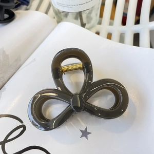 Detailed view of the dark grey bow-shaped hair claw clip with golden metal spring