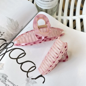 Détail de pinces à cheveux en acrylique rose avec pois foncés et ressorts dorés