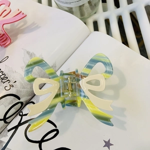 Macro detail of striped acetate bow hair claw clip with a secure golden metal spring