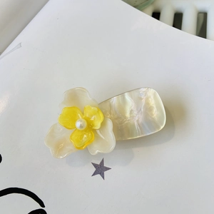 Détail d'une pince à cheveux fleurie 3D avec pétales jaunes et base nacrée