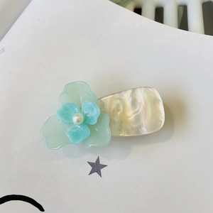 Gros plan d'une pince à cheveux fleur en acétate avec perle sur carte à étoiles
