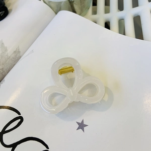 Detail of pearlescent white bow hair claw clip with golden metal spring on magazine