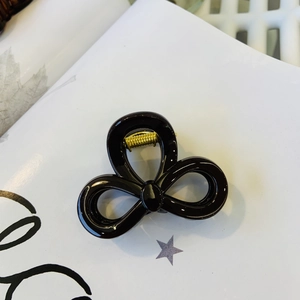 Detail view of glossy black bow hair claw clip with golden metal spring mechanism