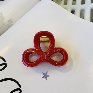 Detailed view of a glossy red resin bow hair claw clip with golden metal spring