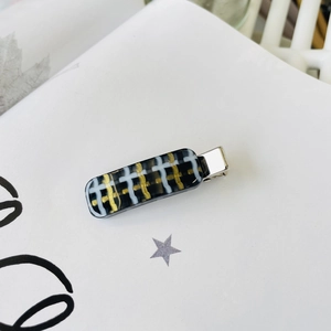 Detailed view of rectangle duckbill hair clip with black and gold plaid patterns