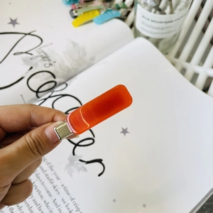 Detail of a bright orange rectangular acrylic hair clip with metallic silver base
