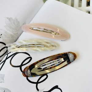 Close-up of three acetate oval hair clips in pink, white grid, and tortoiseshell