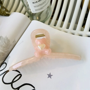 Pink translucent bear hair claw clip with heart detail displayed on a white magazine