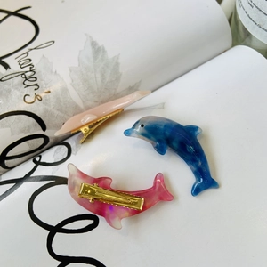 Close-up of three stylish dolphin-shaped hair clips with marble and pearlescent finishes