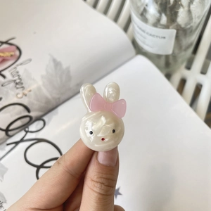 Close-up of a pearlescent cream rabbit hair clip with a pink bow held in hand
