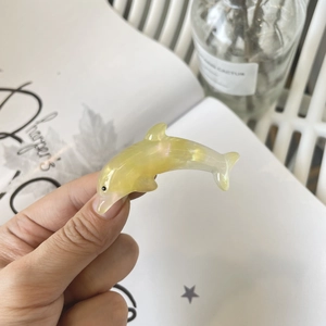 Detail of a pale yellow dolphin hair clip with a pearlescent finish held in hand