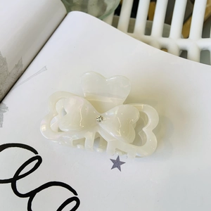 Detailed macro view of a pearl white acetate bow hair claw clip with rhinestone accent