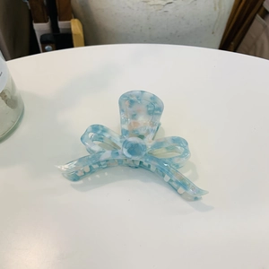 Detail of elegant blue marble acetic acid hair claw clip with bow design and gold logo