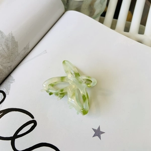 Dettaglio macro del fermaglio a farfalla in acetato verde marmorizzato su sfondo bianco