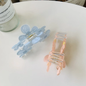 Close-up of two acrylic flower hair claws in light blue and soft peach pink tones