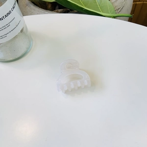 Petite pince à cheveux blanche translucide minimaliste avec dents incurvées sur table