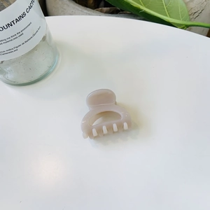 Pince à cheveux demi-cercle beige au design ajouré sur un fond blanc épuré et moderne