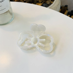 Détail d'une pince à cheveux papillon nacrée blanche avec motifs de cœurs ajourés