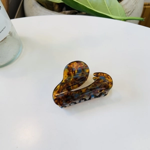 Detail view of tortoiseshell acetate hair claw clip with golden brand logo on a desk