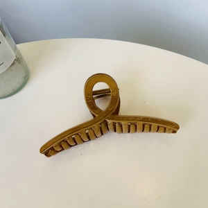 Detailansicht einer großen goldenen Haarklammer mit gedrehtem Schlaufendesign auf weißem Tisch
