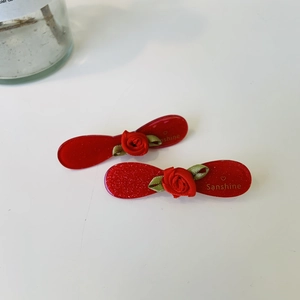 Detail of red acetate hair clips with fabric roses, glitter finish and gold heart logo