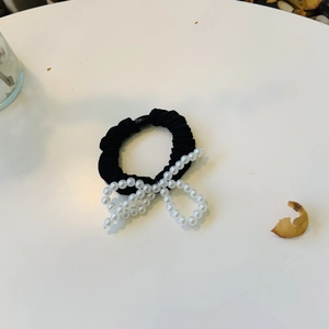 Détail d'un chouchou noir élégant orné d'un nœud décoratif en perles blanches fines