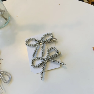 Gros plan de barrettes à cheveux nœud en perles argentées sur carte blanche