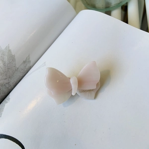 Fermaglio per capelli a farfalla in acetato rosa e bianco con logo dorato su libro