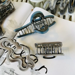 Dettaglio di tre pinze per capelli in acetato con fiocco blu e motivi ondulati grigi