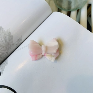 Dettaglio del fermaglio per capelli a fiocco in acetato marmorizzato rosa con logo oro
