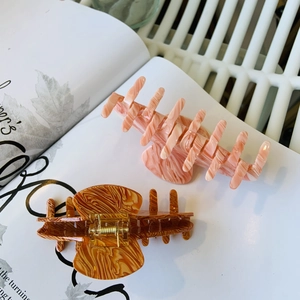 Vue détaillée de deux grandes pinces à cheveux texturées en rose pêche et brun ambre