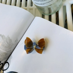 Dettaglio di un fermaglio per capelli a farfalla in acetato marrone con logo dorato